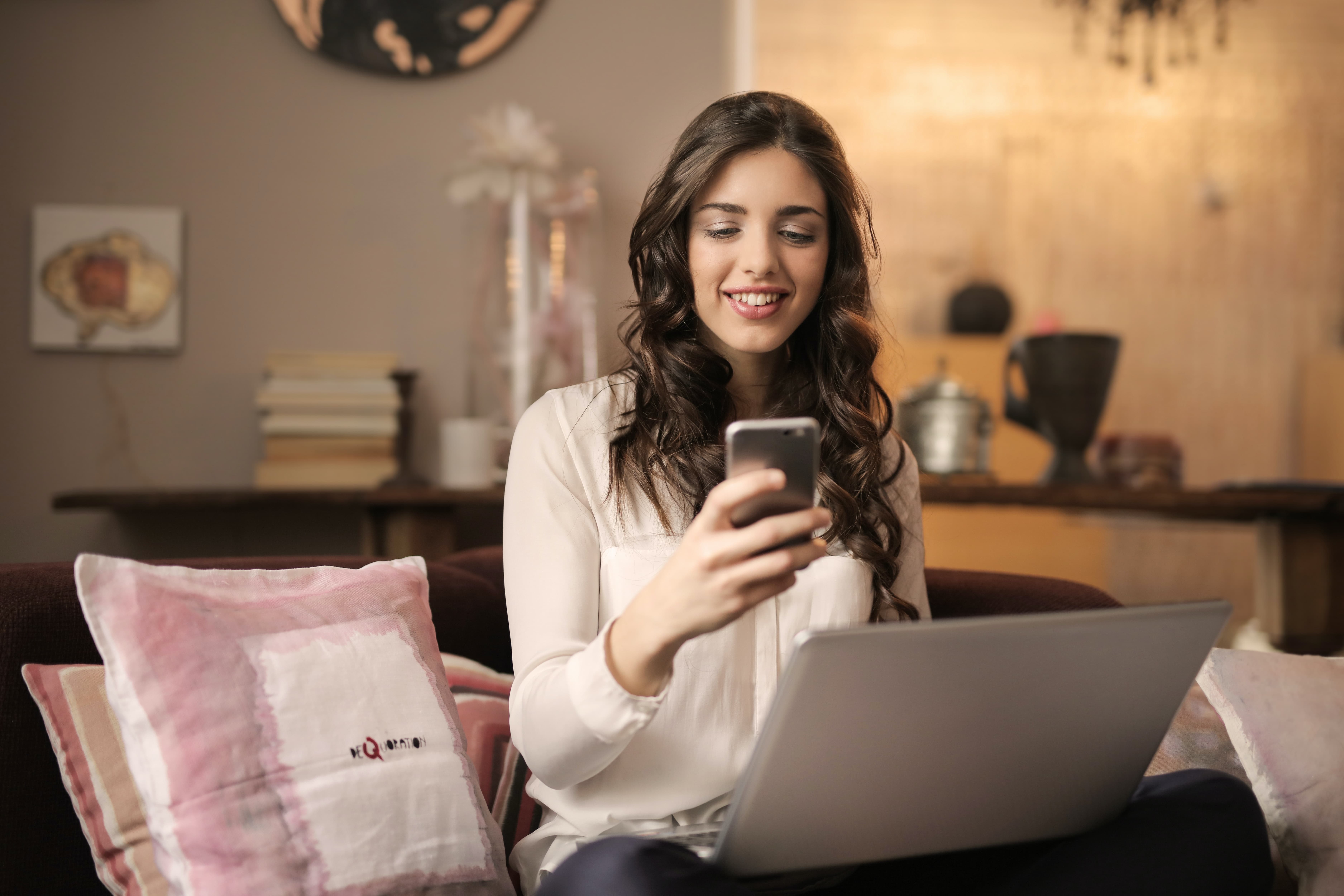 woman-sitting-on-sofa-while-looking-at-phone-with-laptop-on-920382.jpg